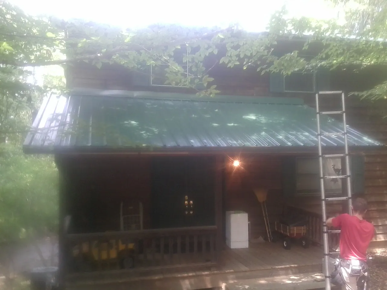 Worker on a ladder at the green porch roof of a wooded cabin in Westminster